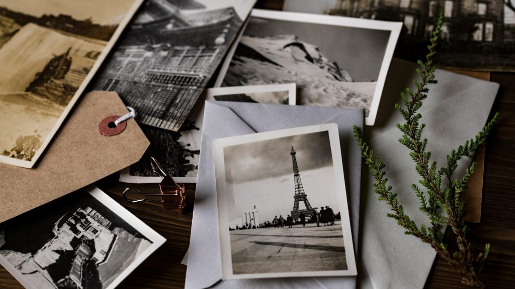 A collection of black and white vintage photos scattered on a wooden surface including a postcard of the eiffel tower and a green sprig